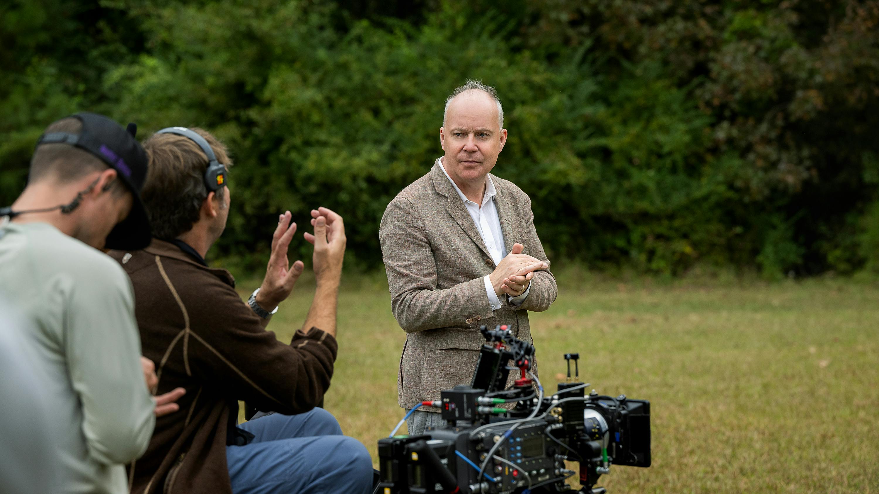 David Yates on the set on Pain Hustlers. He wears a white shirt and a khaki blazer and rubs his hands together. 