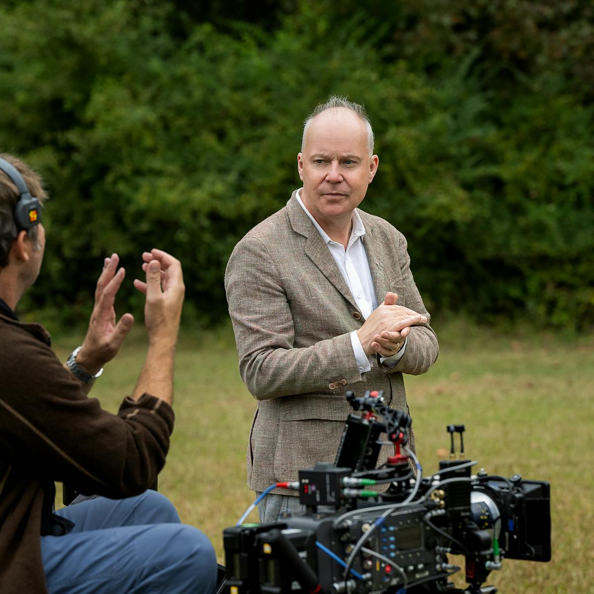 David Yates on the set on Pain Hustlers. He wears a white shirt and a khaki blazer and rubs his hands together. 