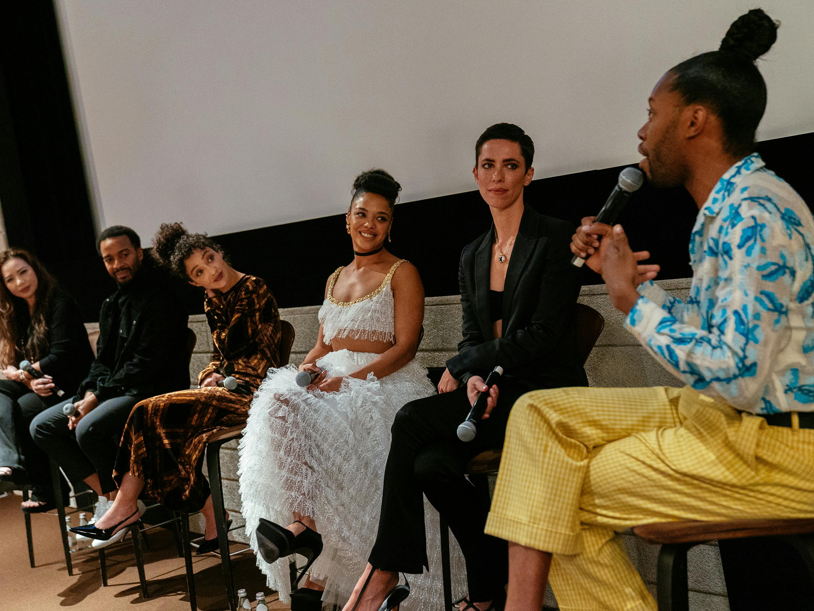 Nina Yang Bongiovi, André Holland, Ruth Negga, Tessa Thompson, Rebecca Hall, and Jeremy O. Harris talk to each other from atop hightop chairs.  