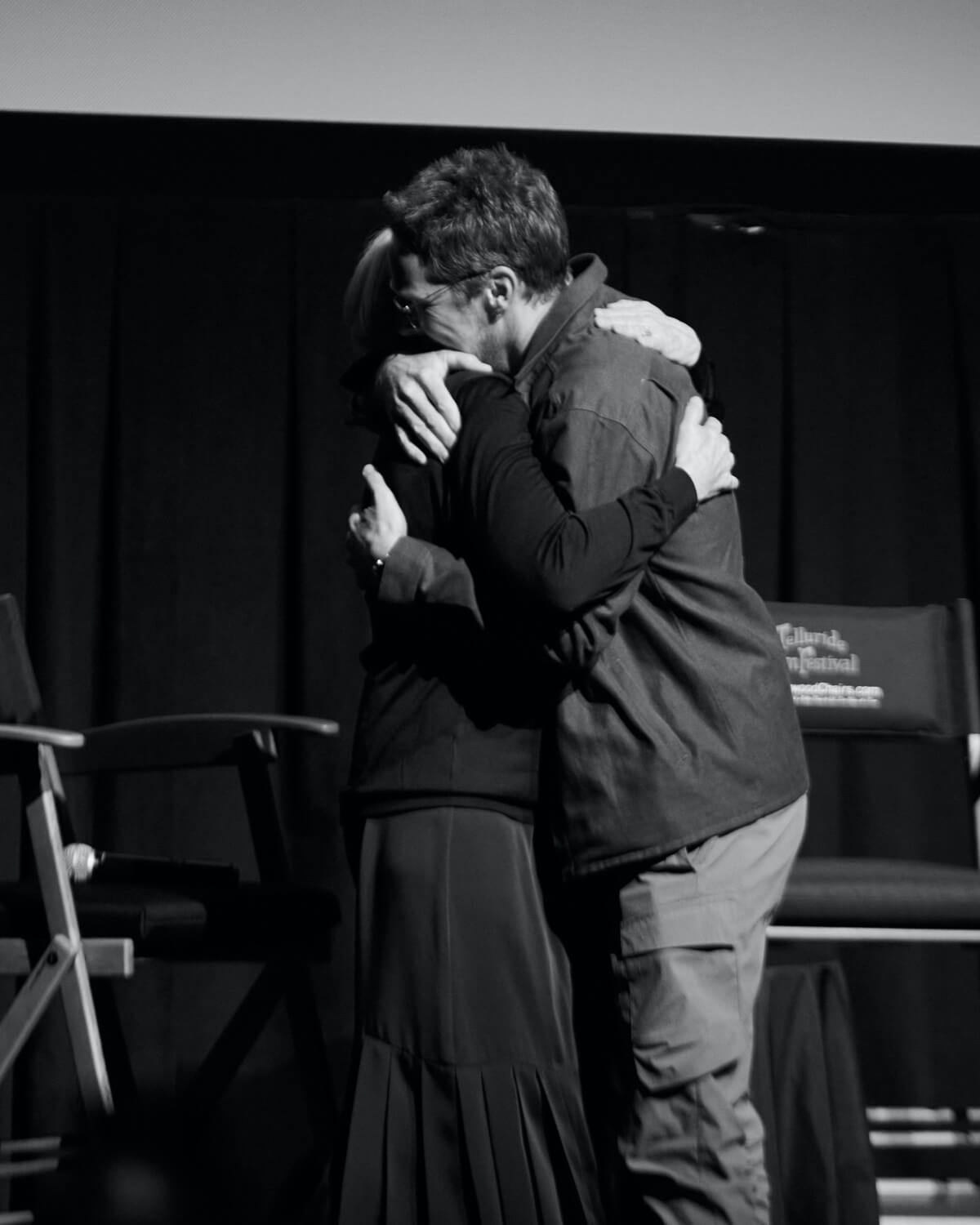 A black and white shot of Jane Campion and Benedict Cumberbatch at Telluride Film Festival, 2021, embracing each other on a stage.