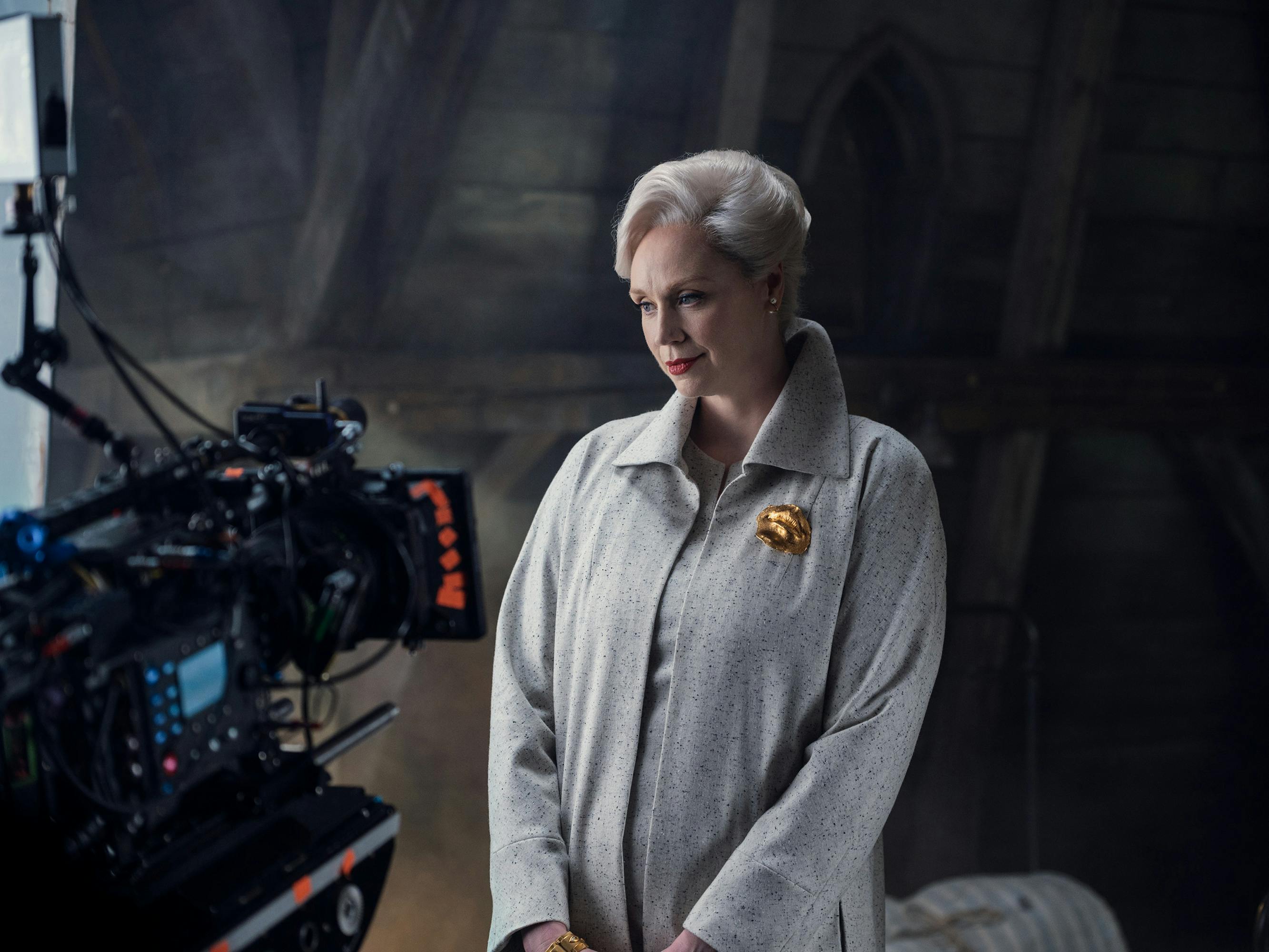 Larissa Weems (Gwendoline Christie) wears a grey coat with a gold brooch behind the scenes of Wednesday.