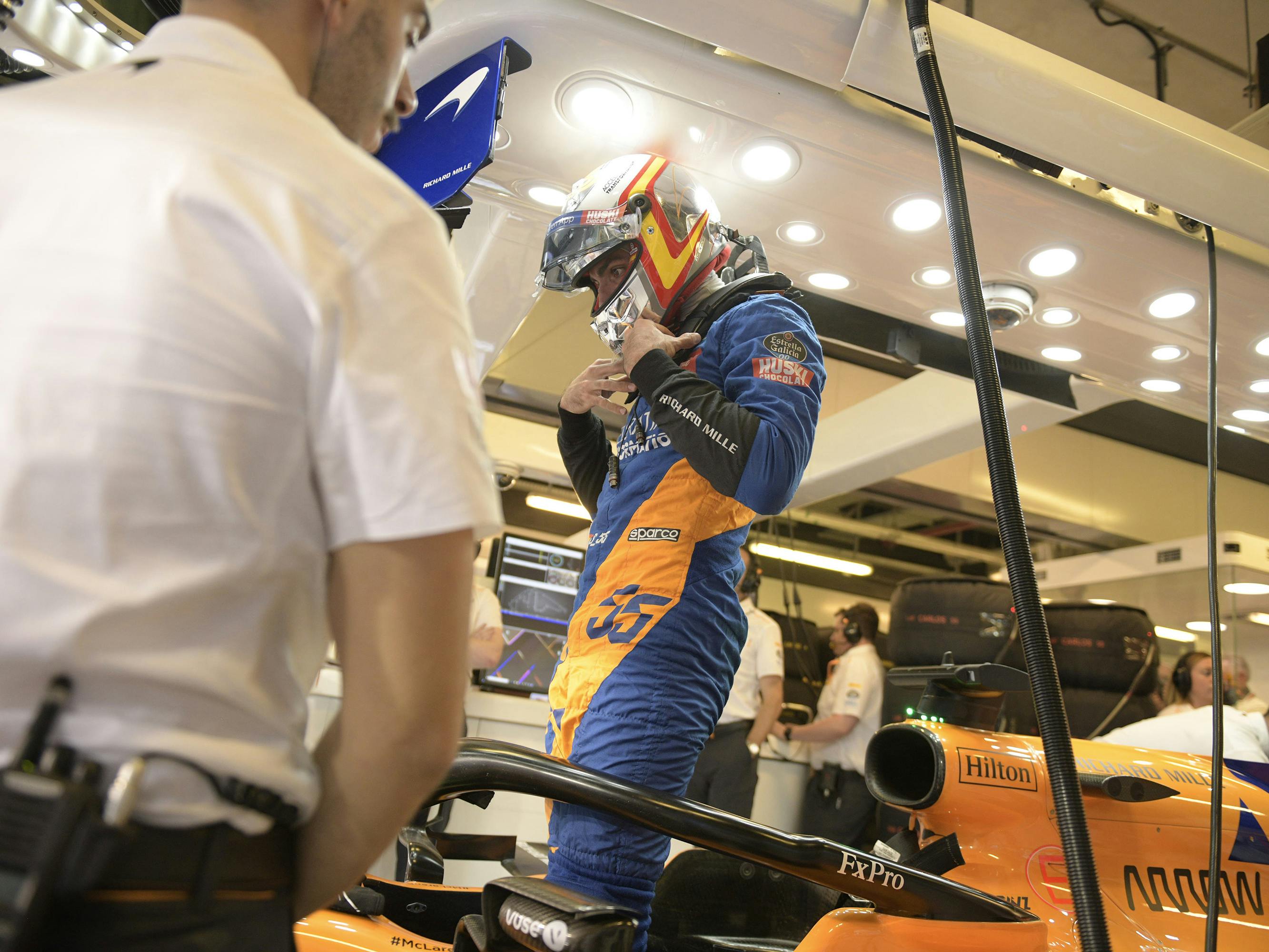 Carlos Sainz Jr. wears a blue-and-orange racing uniform and matching helmet in this behind-the-scenes shot.