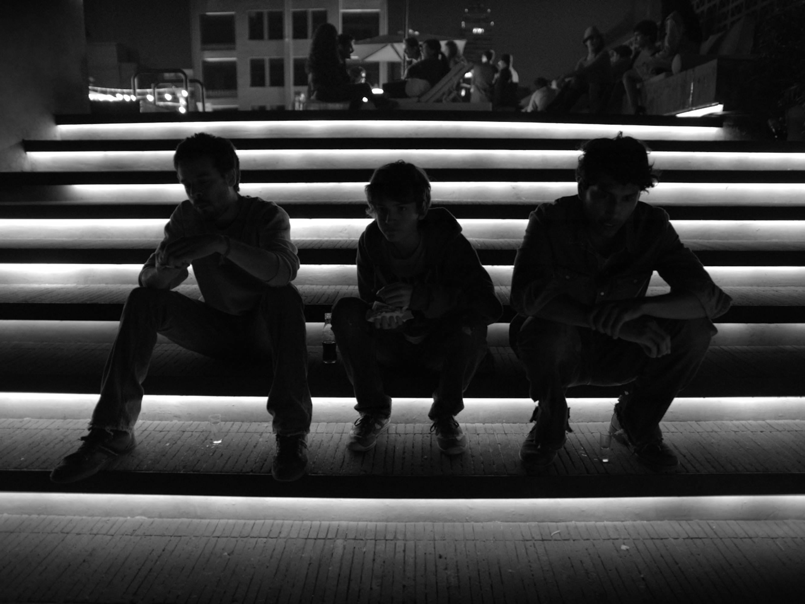 Three dimly-lim characters from Güeros sit on dark steps.