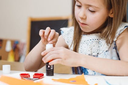 Child using glue and scissors on scrapbook