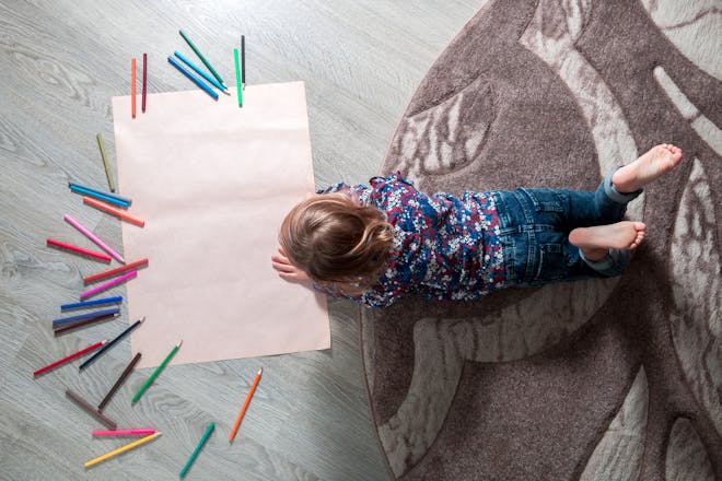 A child lying on the floor drawing on a big piece of paper