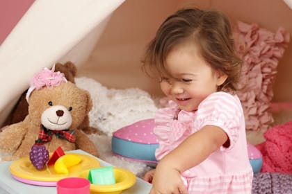 Toddler girl playing with teddy bear and toy food at tea party game