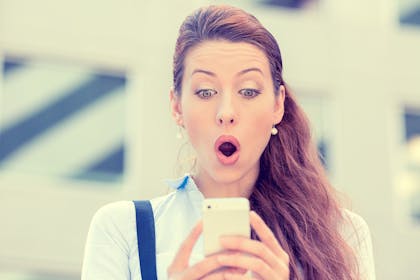 woman pulling a shocked face looking at her mobile phone