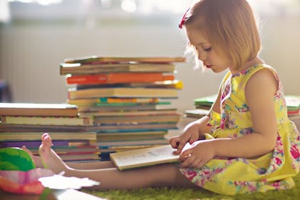 Girl sat on the floor reading next to a pile of books