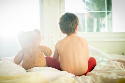 child sat on bed with teddy bear
