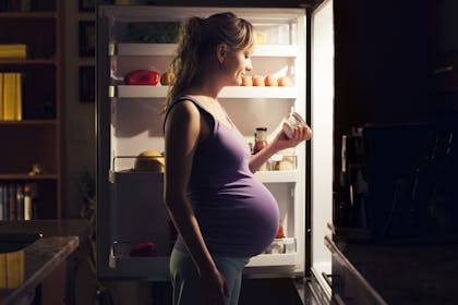 pregnant woman looking at food in fridge