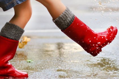 Child in red wellies splashes through puddles