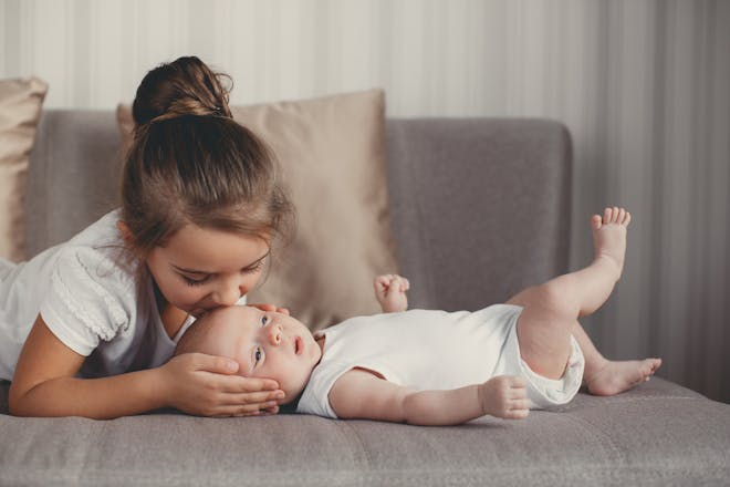 girl in white kissing baby on forehead while lying on a sofa
