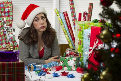 woman surrounded by christmas presents and wrapping paper looking exhausted