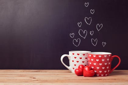 Two mugs with hearts on them, in front of blackboard with chalk hearts