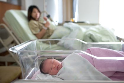 newborn baby girl asleep in hospital with mum in the background