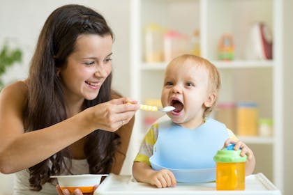 smiling woman spoon feeding her baby in high chair