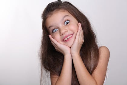 Child smiling, her hands cupping her face