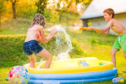 children playing in garden in paddling pool with water pistol