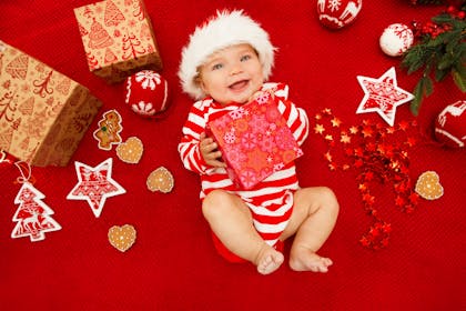 baby in santa hat surounded by christmas presents and decorations