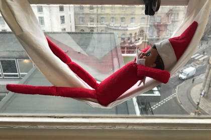 Elf on the Shelf sleeps in window hammock made out of toilet paper