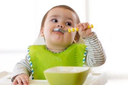 baby girl eating with spoon and bowl