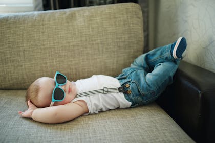 Baby lying on sofa wearing shades and jeans