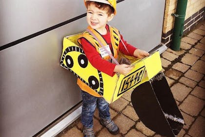 Kid dressed in Bob the builder costume with hi-vis, hard hat and cardboard forklift