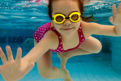 Little girl with goggles under water at swimming pool
