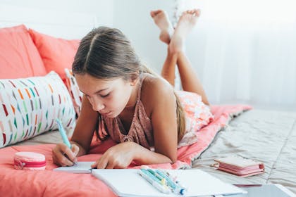Child writing in her journal on her bed