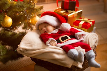 baby in santa suit next to christmas tree
