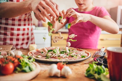 father and daughter making pizza with mushrooms, ham and greens