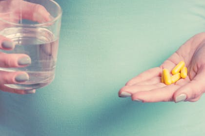 Woman holding glass of water and some folic acid pills