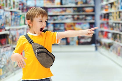 child screaming and pointing at toy in shop