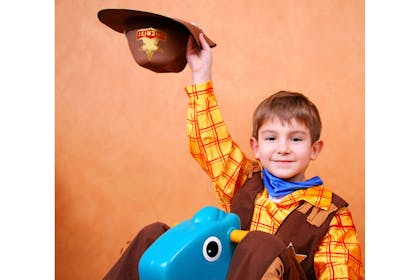 Boy in Woody costume holds cowbody hat above head