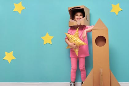Little girl dressed up as astronaut with cardboard rocket and star 