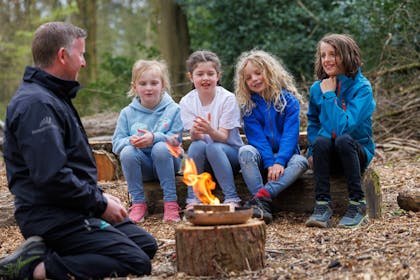 Four kids enjoy an activity with a Ranger about fire building on a Forest Holidays break