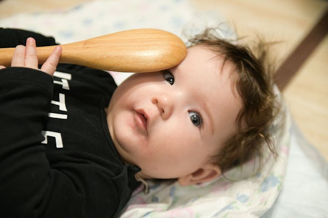 baby lying down holding a wooden spoon against face