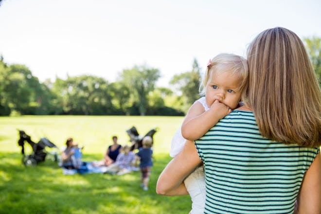woman holding baby looking at other mums in park
