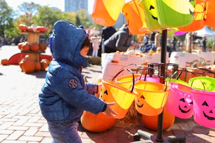A toddler in a duffel coat picks out a trick or treat bucket at a Halloween festival