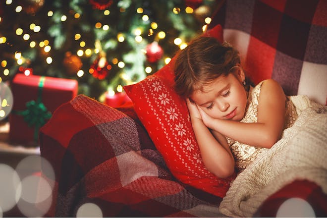 Little girl sleeping beside the Christmas tree 