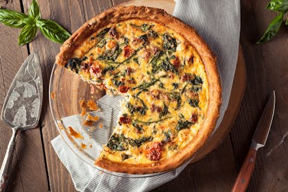Quiche on wooden board with large slice cut out of it