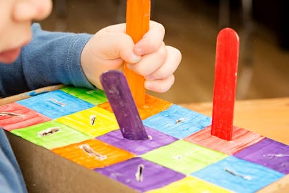 Child placing coloured lolly sticks into a homemade colour sorter toy