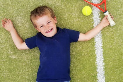 Boy lying on tennis court with racket and ball