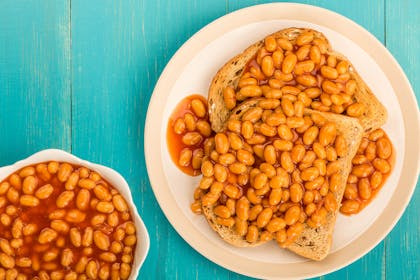 Plate of baked beans on toast next to bowl of baked beans