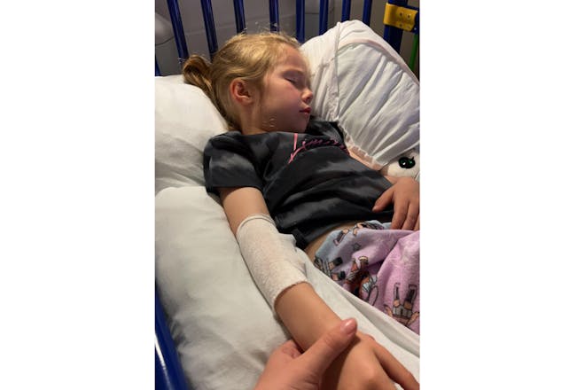 Madison asleep in hospital bed with mum holding her hand