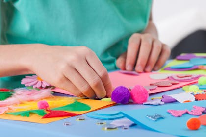 Child crafting with pom poms and feathers