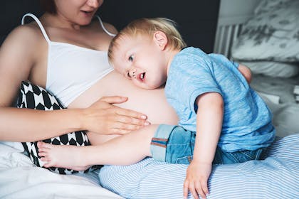 Toddler lying on mum's pregnant tummy and listening to heartbeat