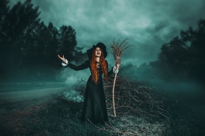 An angry witch with her broomstick standing in the woods
