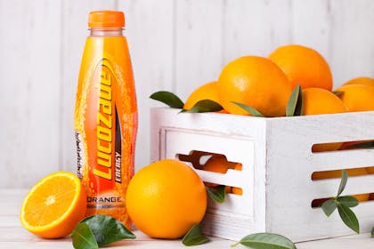 Bottle of orange Lucozade next to crate of oranges