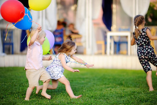 young children playing tag in garden holding balloons